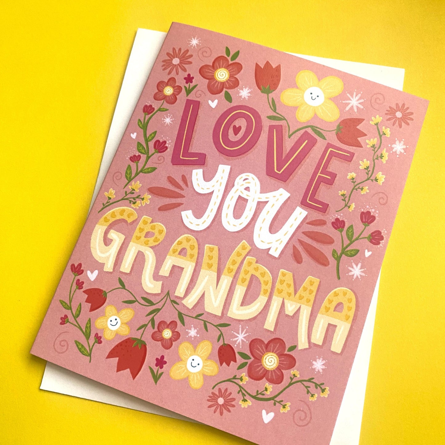 A pink greeting card with a floral border and the text 'LOVE you GRANDMA' in a colorful, stylized font.