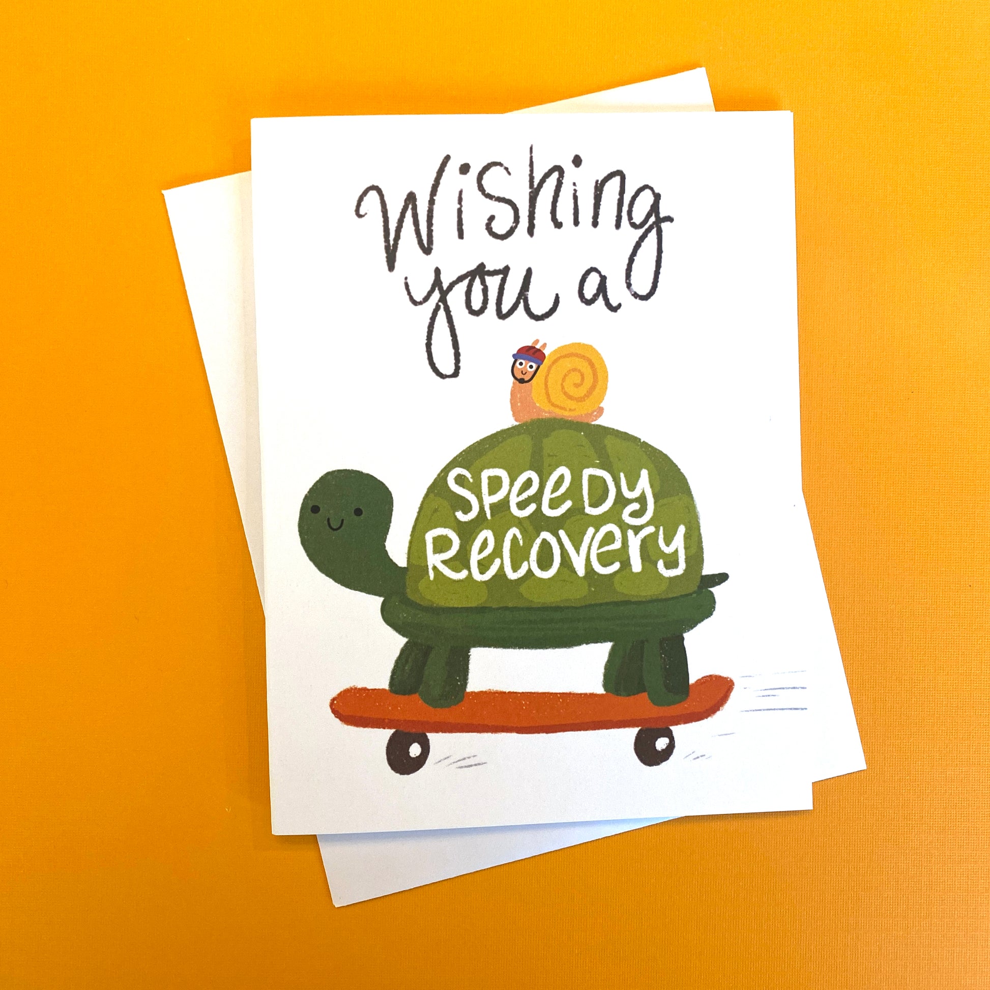 A get well greeting card with a cute turtle on a skateboard. It reads "wishing you a speedy recovery". There is also a snail on the turtle. 