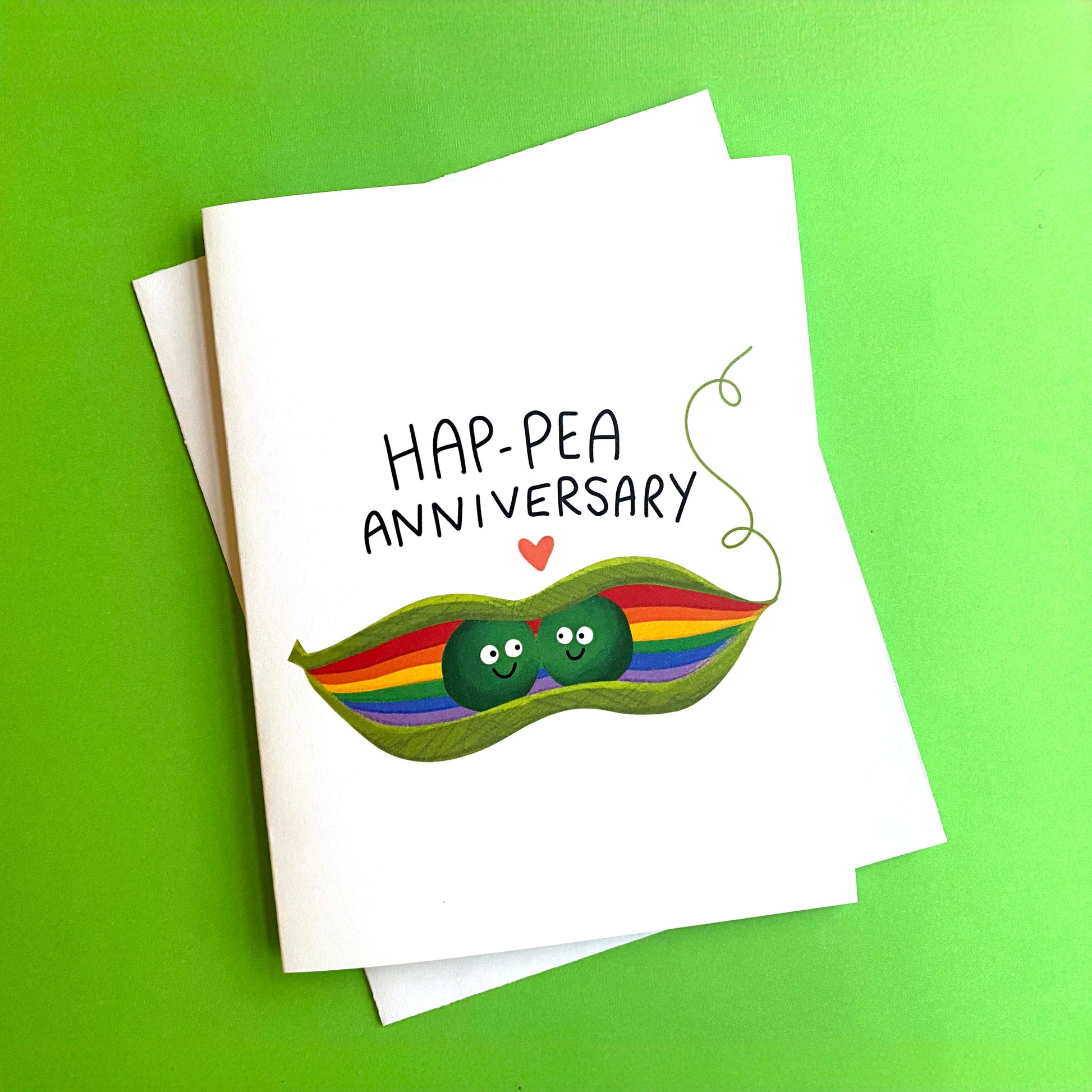 An anniversary card for an LGBTQ+ couple that has two cute peas in a rainbow pea pod. The cards has the pun "Hap-pea Anniversary"> Size A2 greeting card with a blank inside and white envelope.