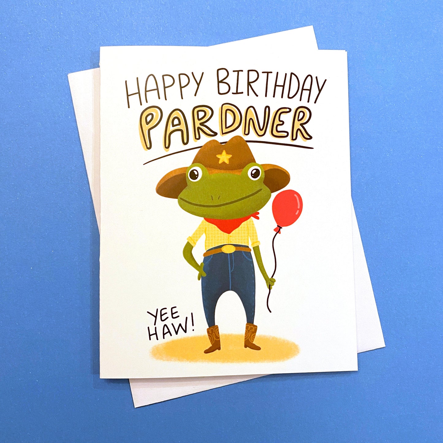 This cute cowboy frog is a funny way to say happy birthday PARDNER. Yeehaw! Size A2 greeting card (4.25&quot; x 5.5&quot;) with envelope- Blank Inside. All cards are designed and Illustrated by Anna Fox and are printed  in Denver, CO.