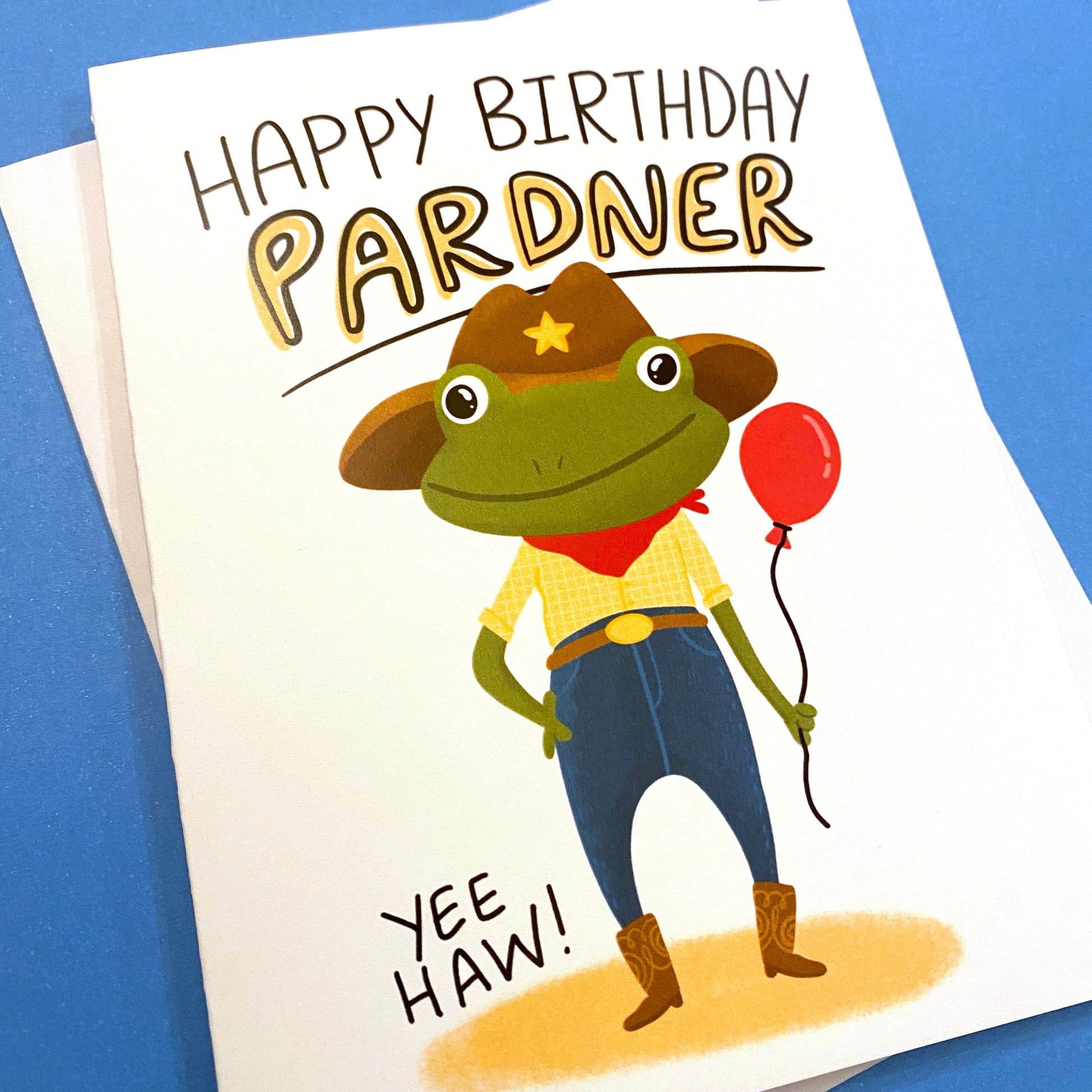 This cute cowboy frog is a funny way to say happy birthday PARDNER. Yeehaw! Size A2 greeting card (4.25&quot; x 5.5&quot;) with envelope- Blank Inside. All cards are designed and Illustrated by Anna Fox and are printed  in Denver, CO.