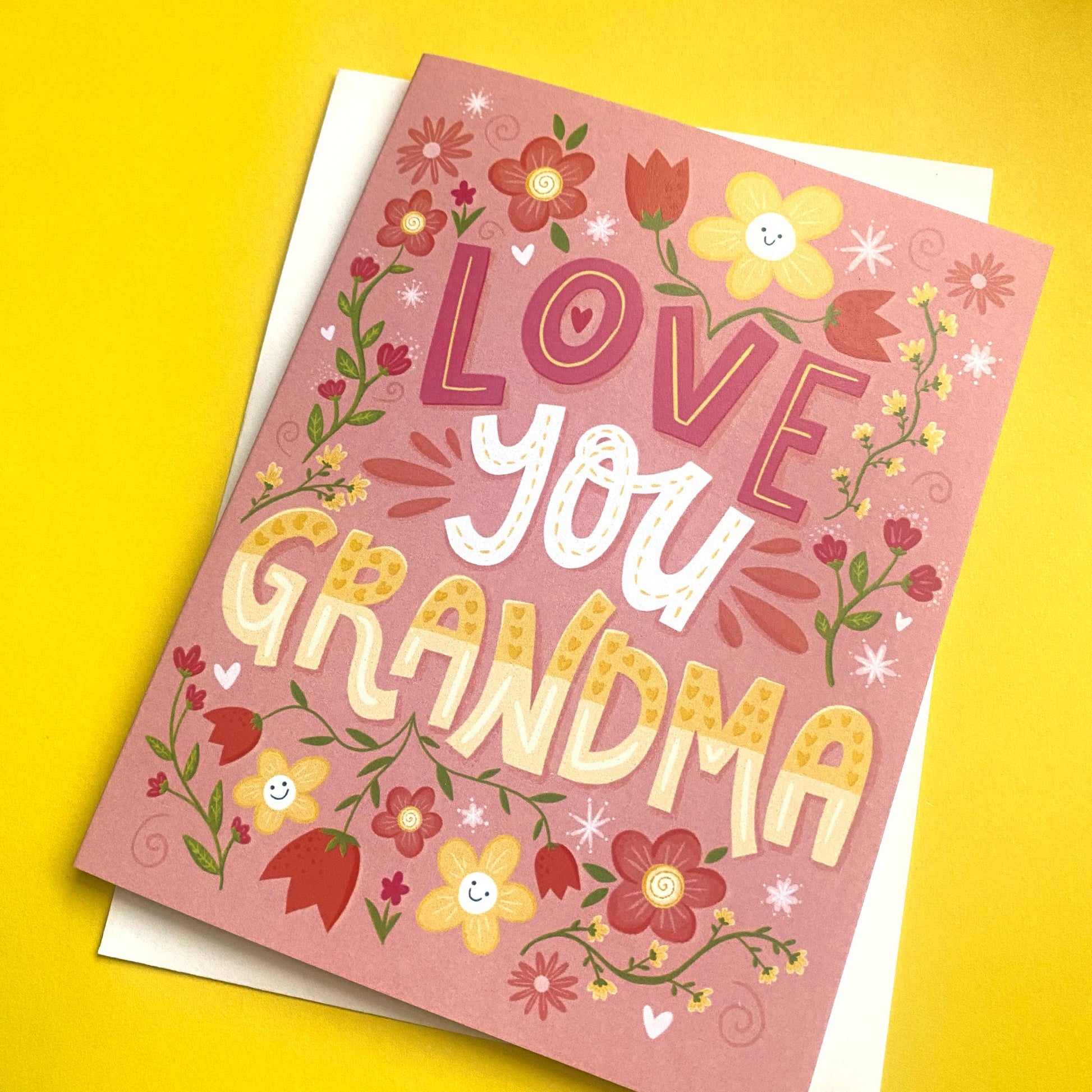 A pink greeting card with a floral border and the text &#39;LOVE you GRANDMA&#39; in a colorful, stylized font.